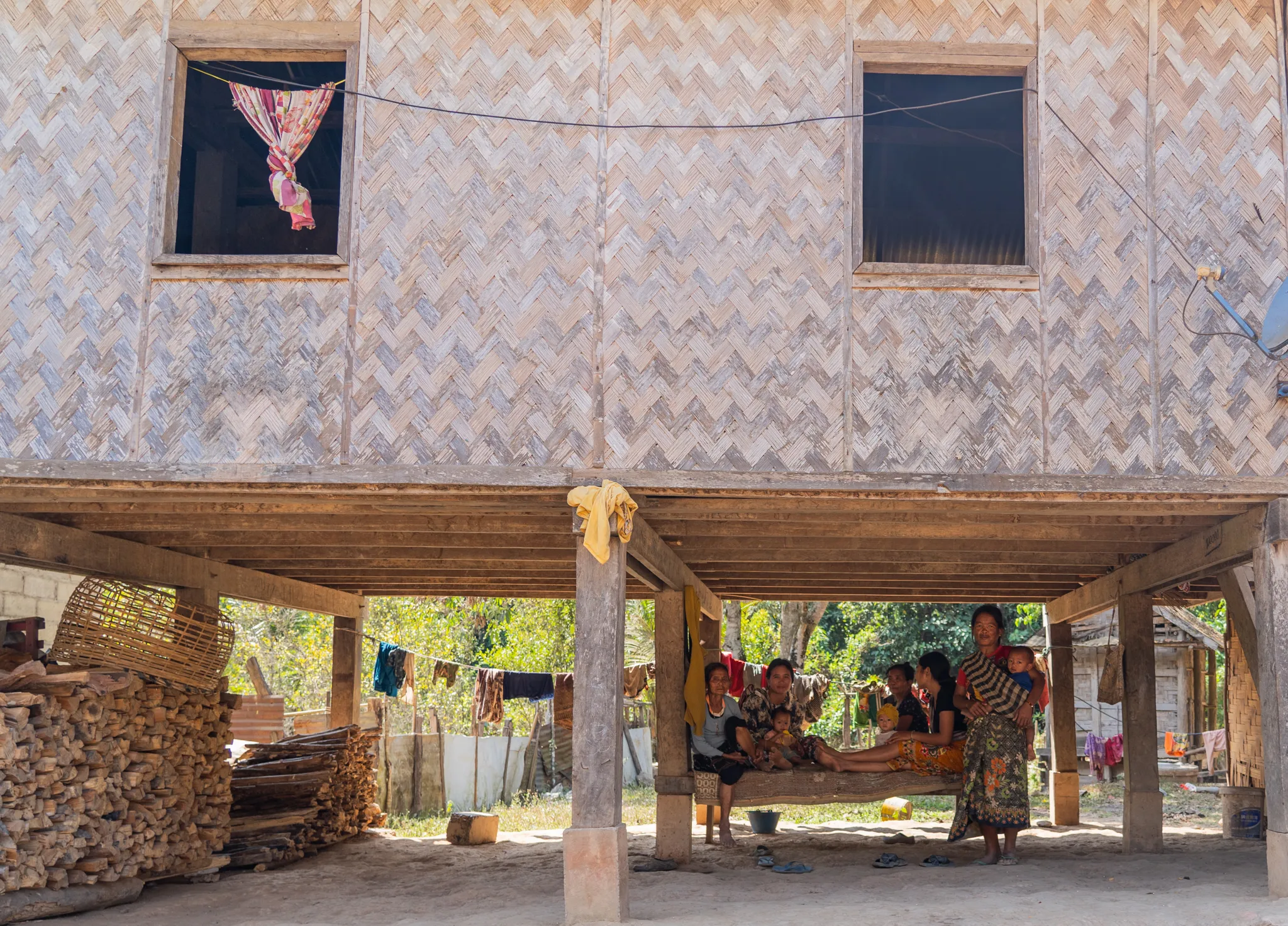 Extended family gathers beneath a stilted bamboo house