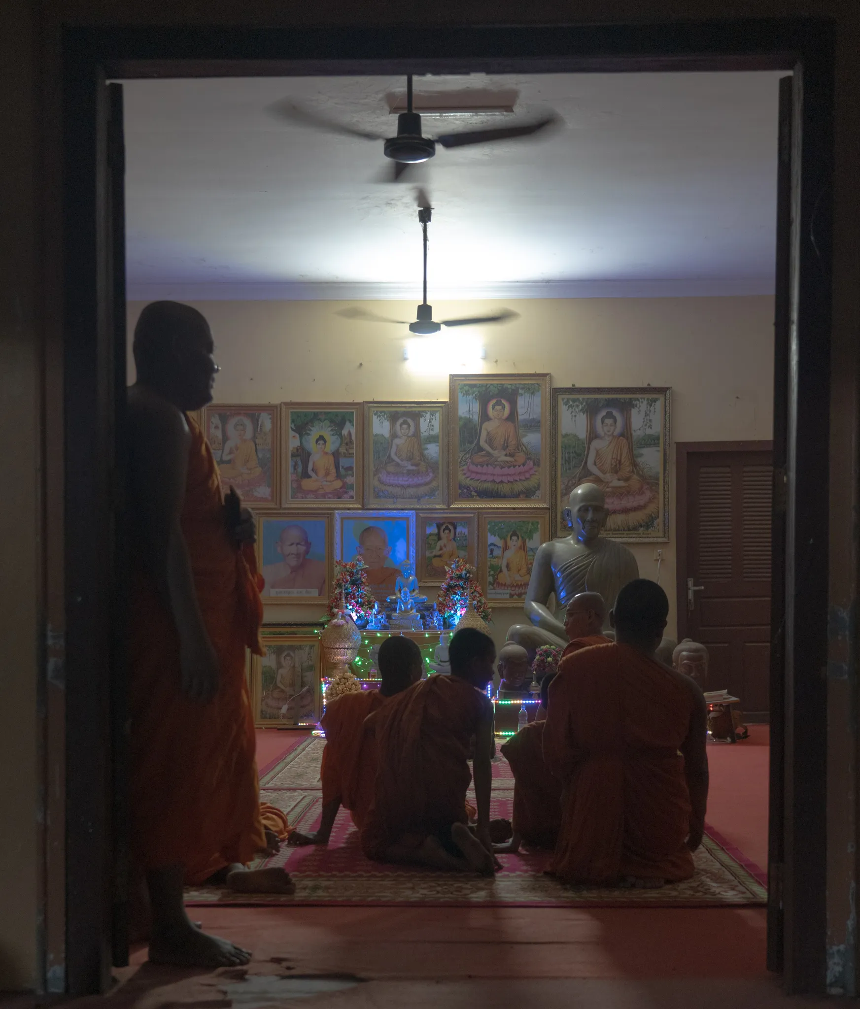 Monks kneeling before a wall of Buddha portraits