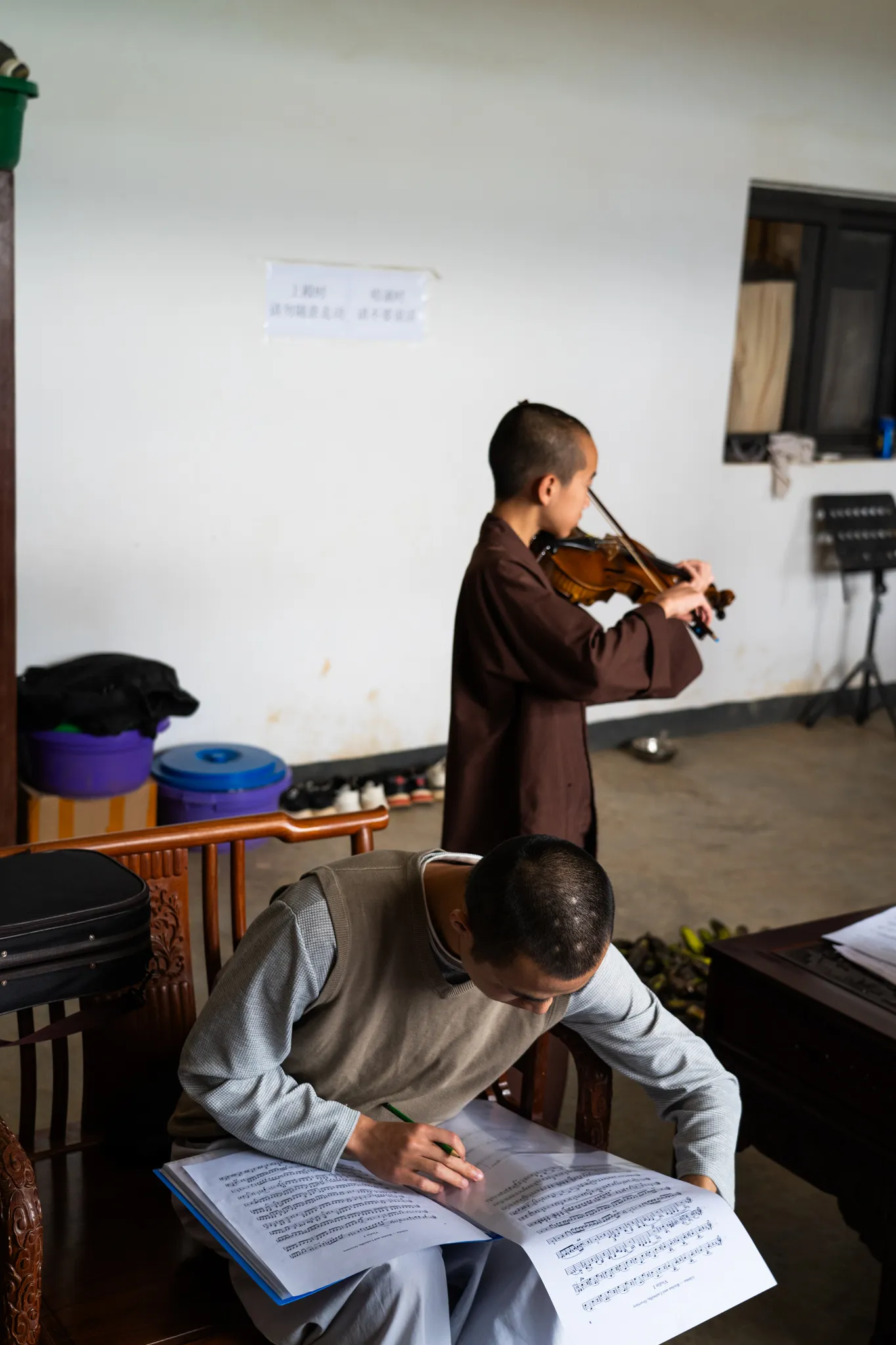 Monk practices violin while another marks up sheet music