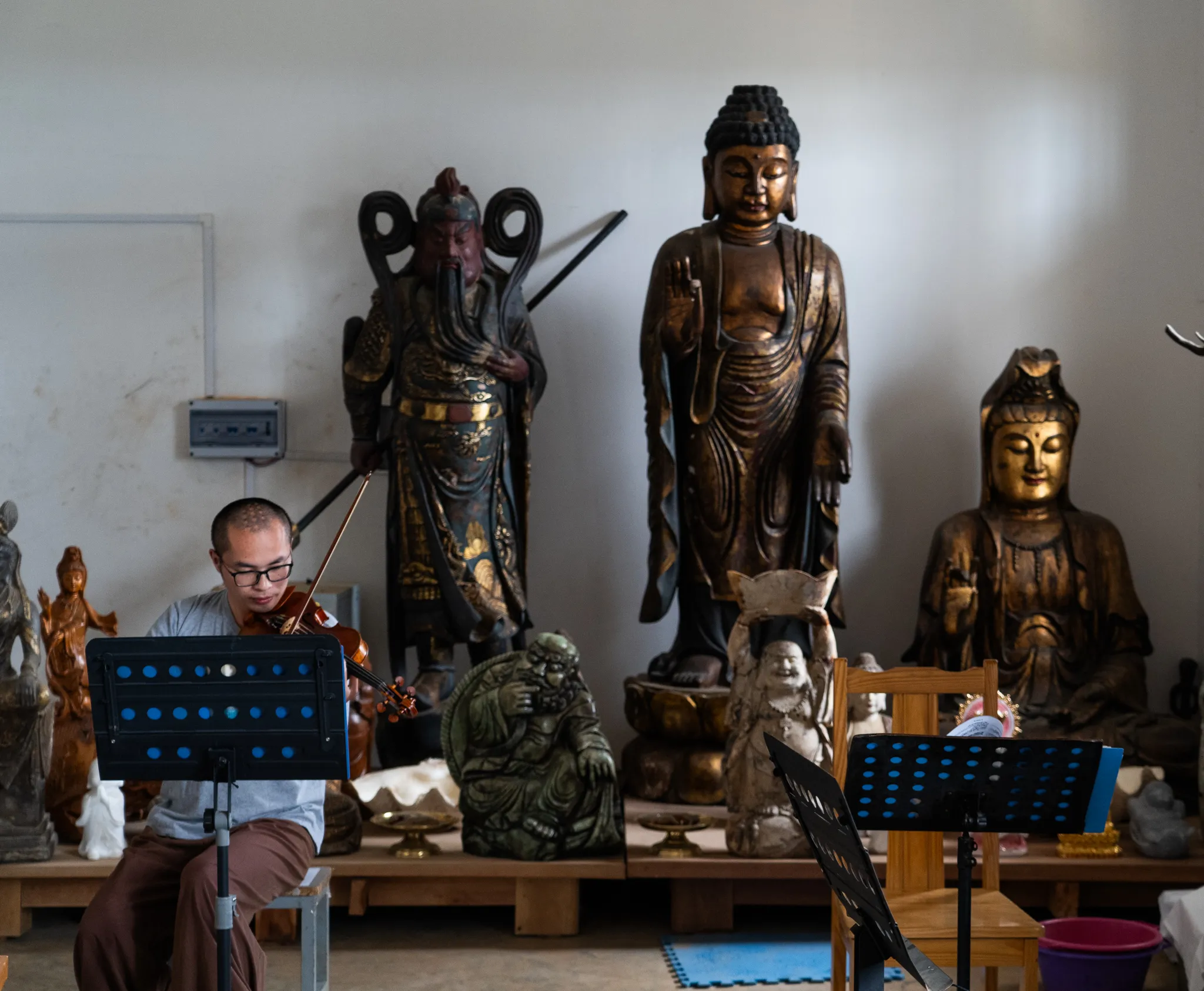 A young monk rehearses violin beside towering gilded statues