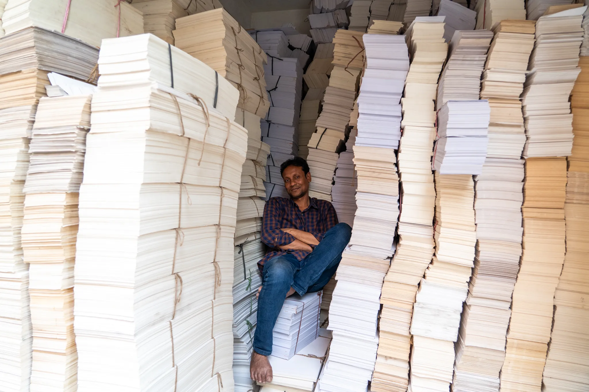 Seated amid stacks of blank paper, India