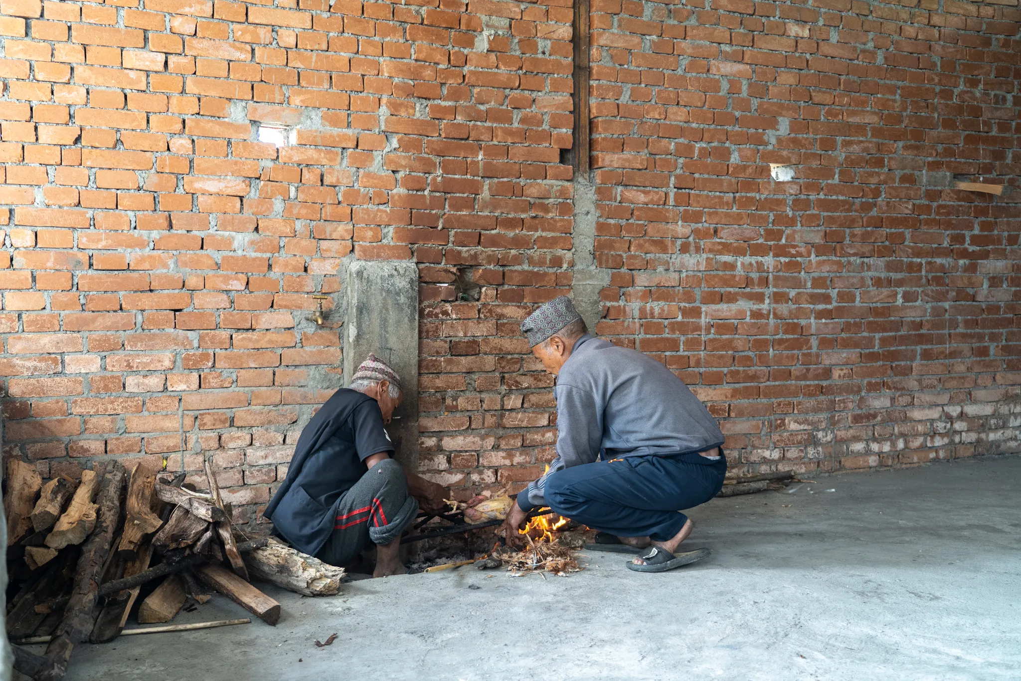 Two men tending a fire against a brick wall