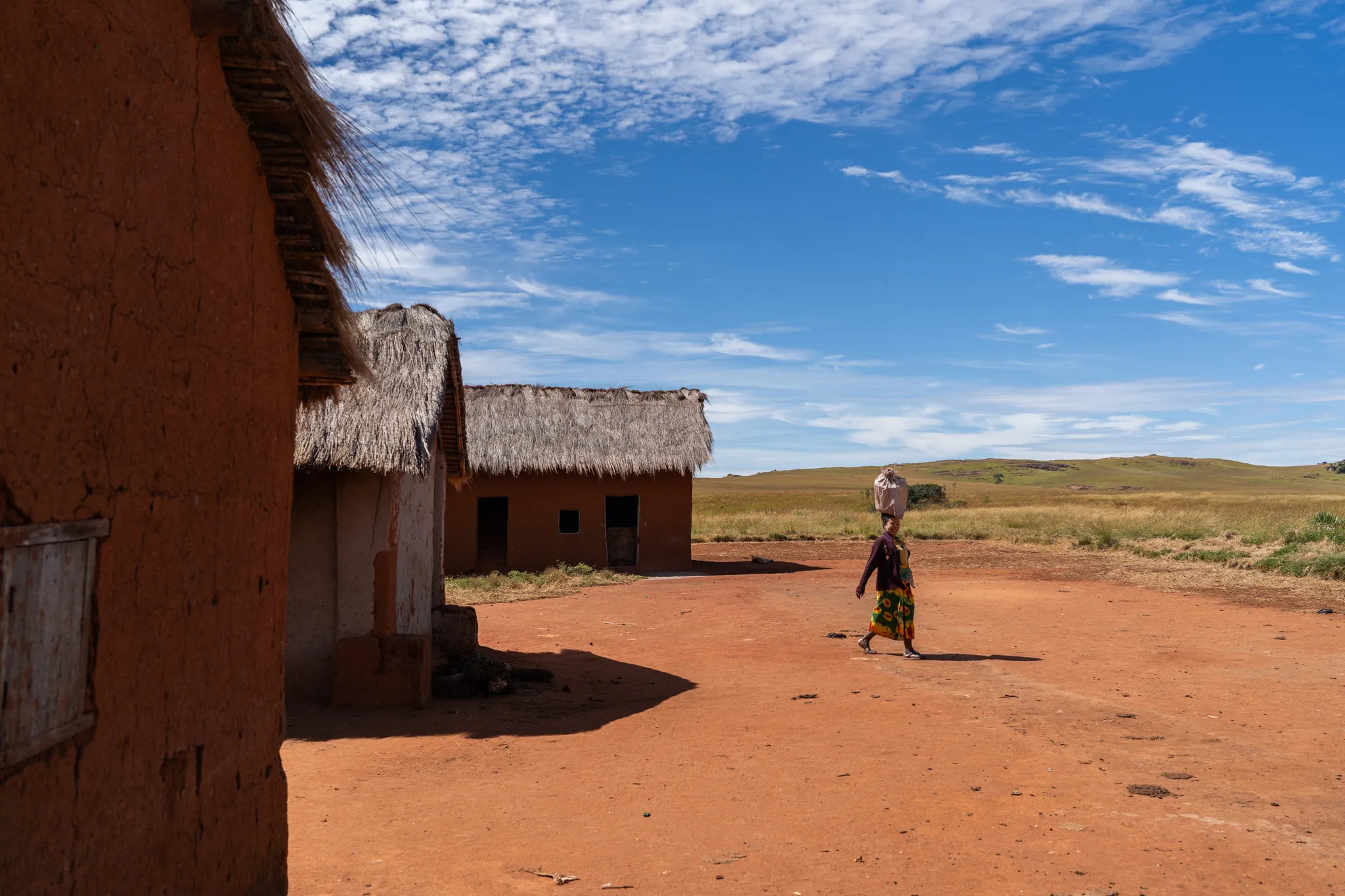 Woman carrying a basket past thatched houses