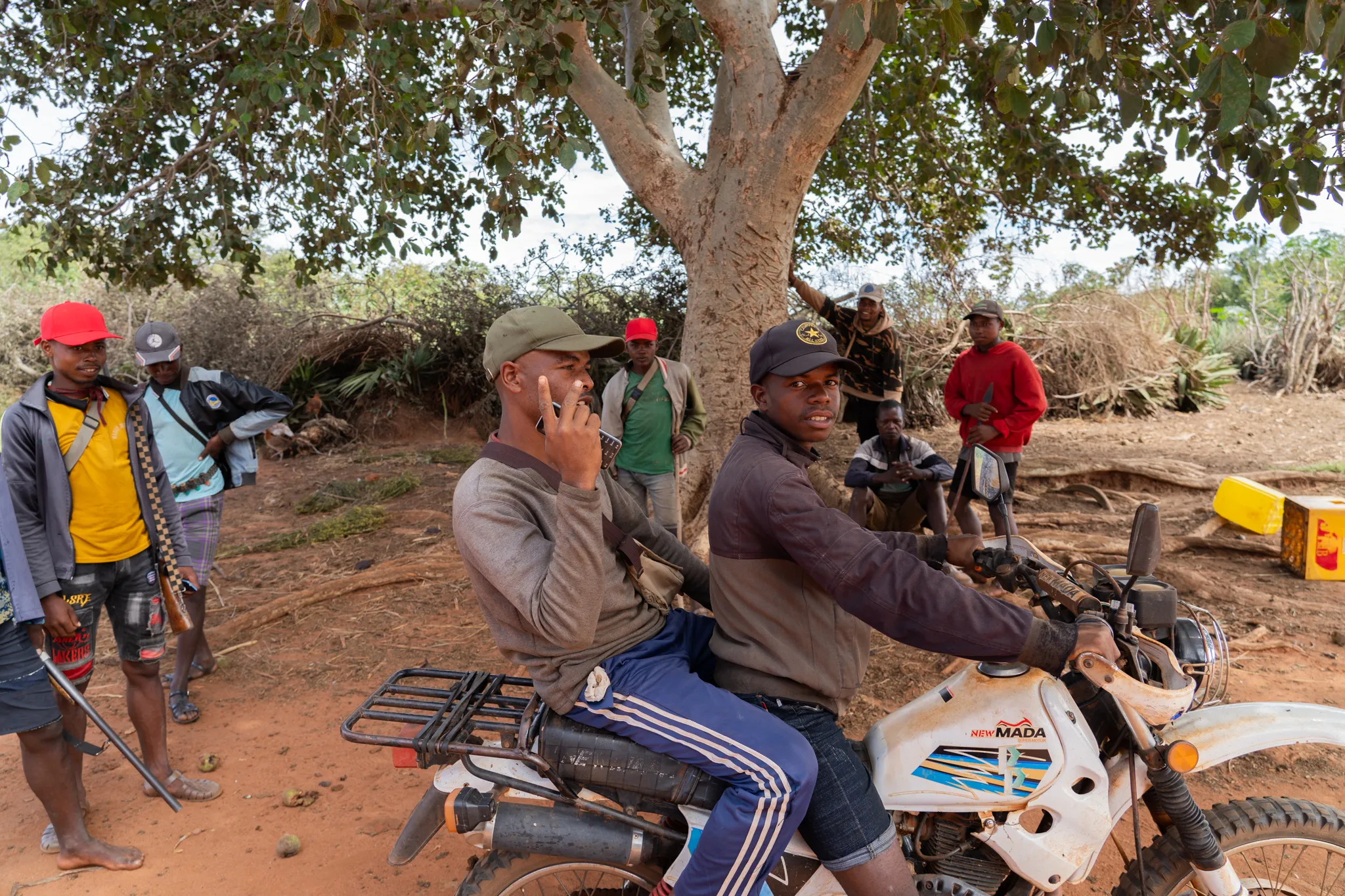 Men gathered under a tree with a motorbike