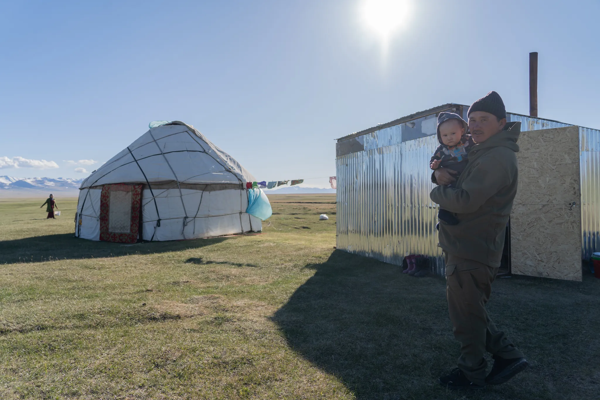 Man and his baby in front of their yurt, his wife approaches in the distance, Kyrgyzstan
