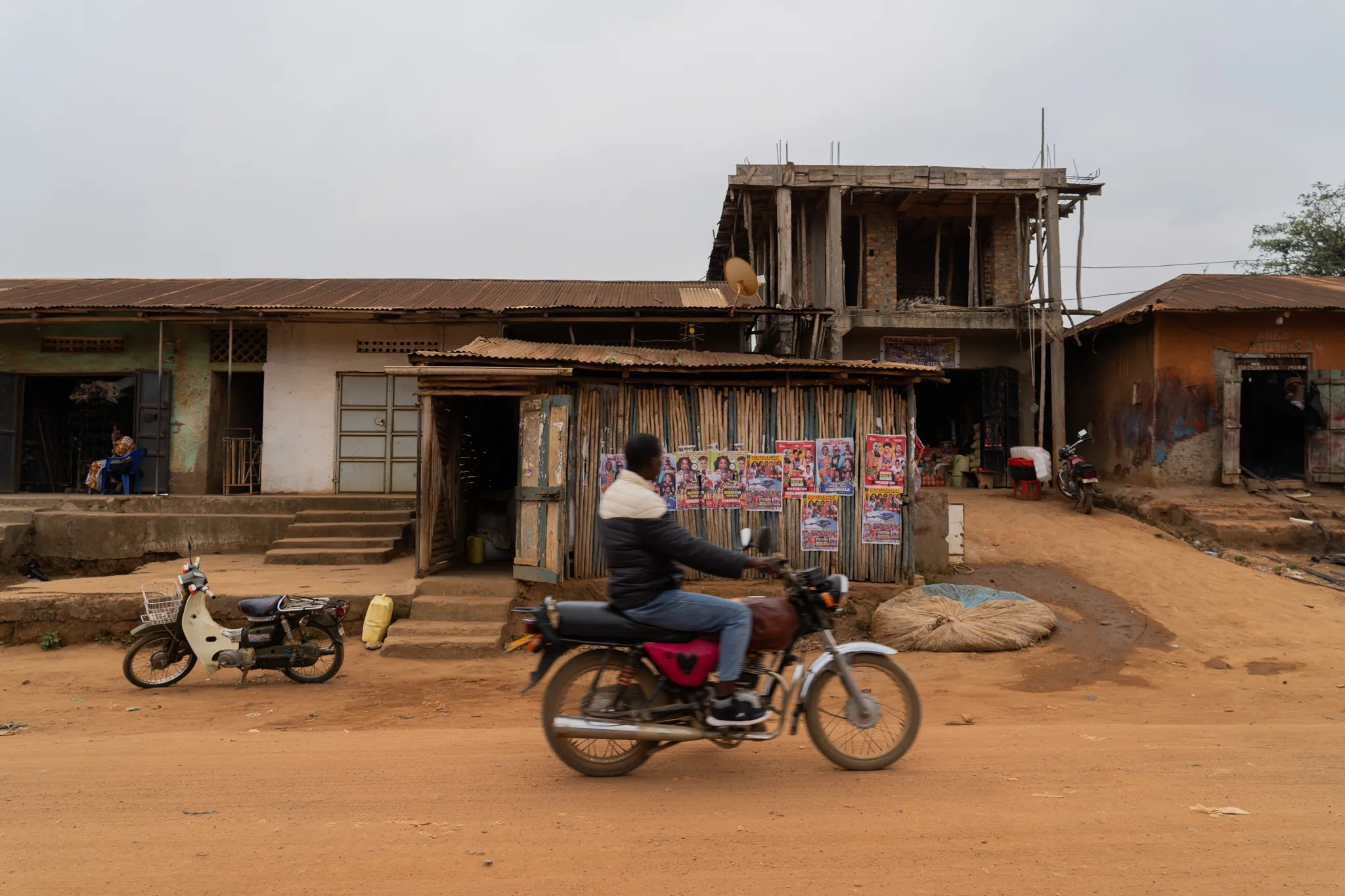 Motorbike passing a poster-plastered roadside shop, Uganda