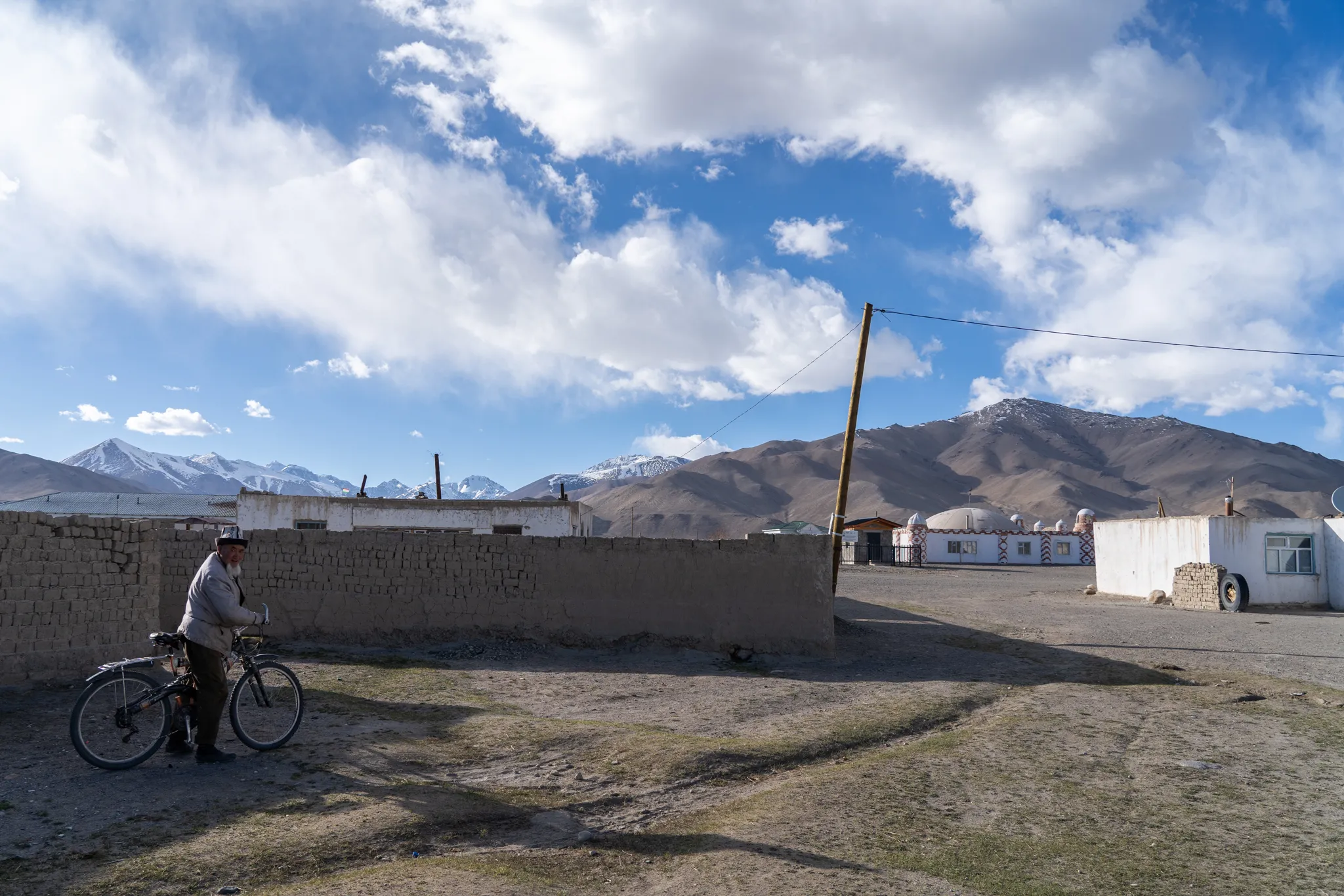 Elderly man with bicycle beside mudbrick wall, Kyrgyzstan