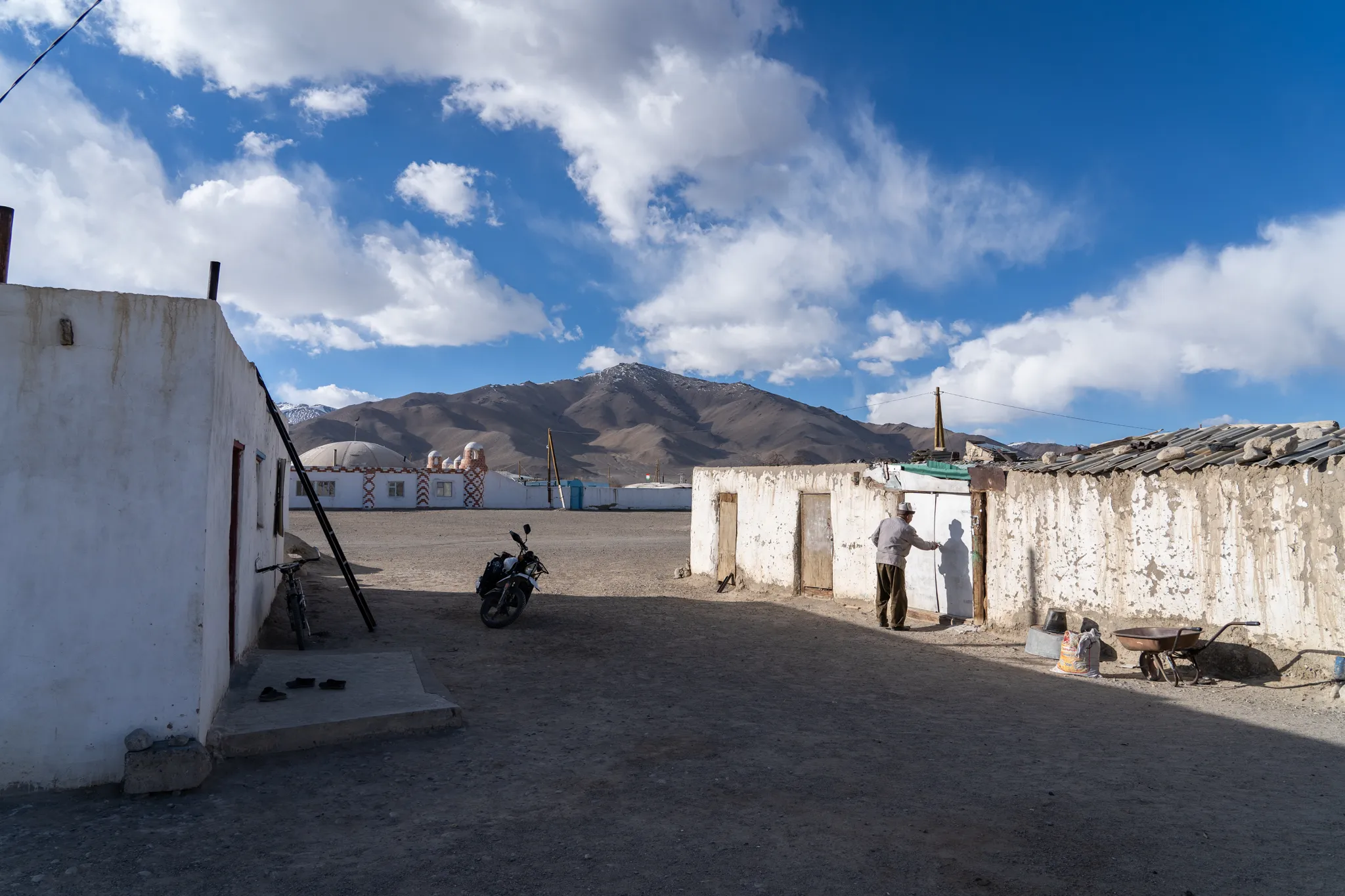 Man at a doorway between whitewashed courtyard walls, mountains beyond, Tajikistan