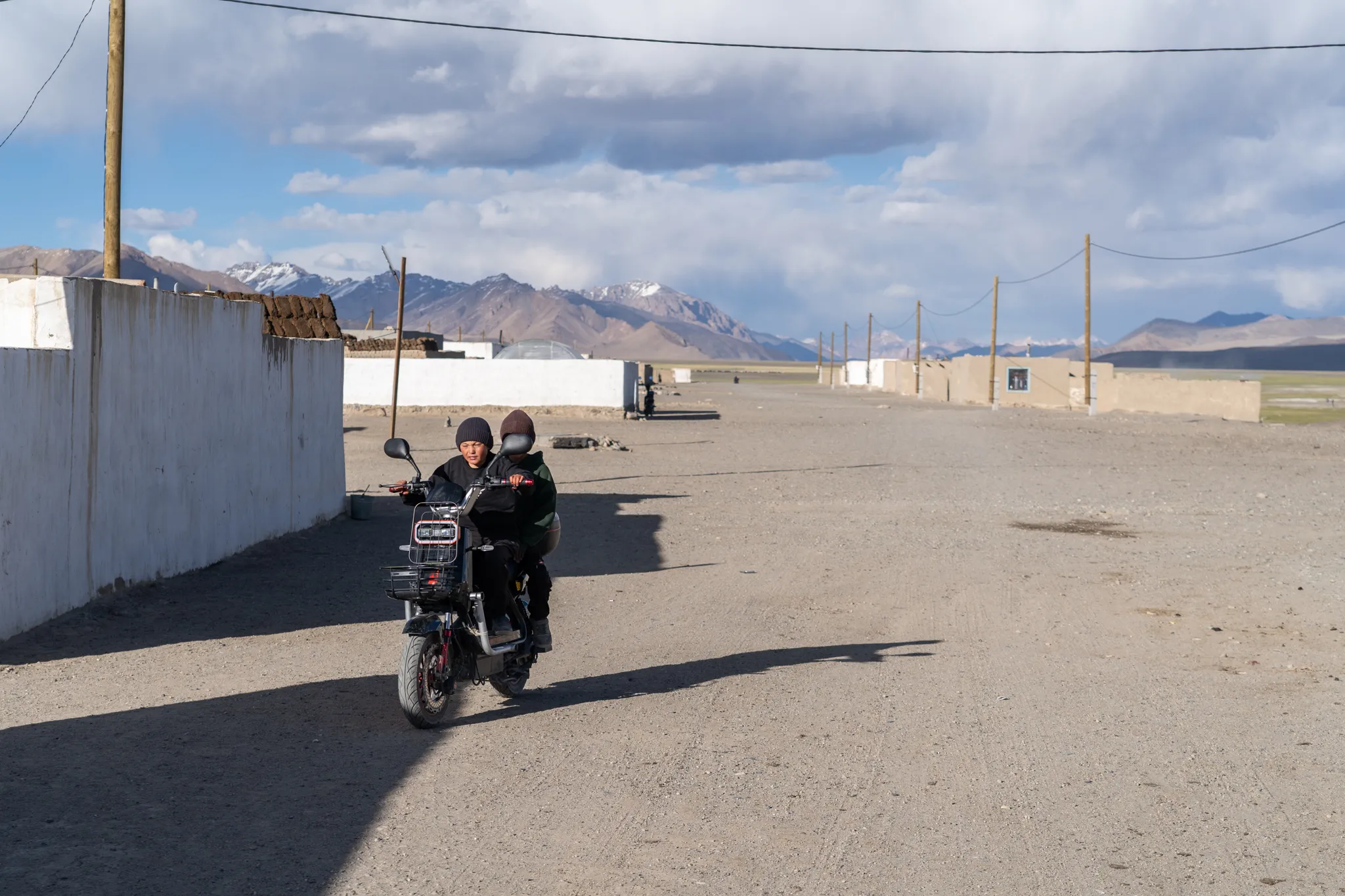 Two boys riding an electric motorbike down a dusty village road, Tajikistan