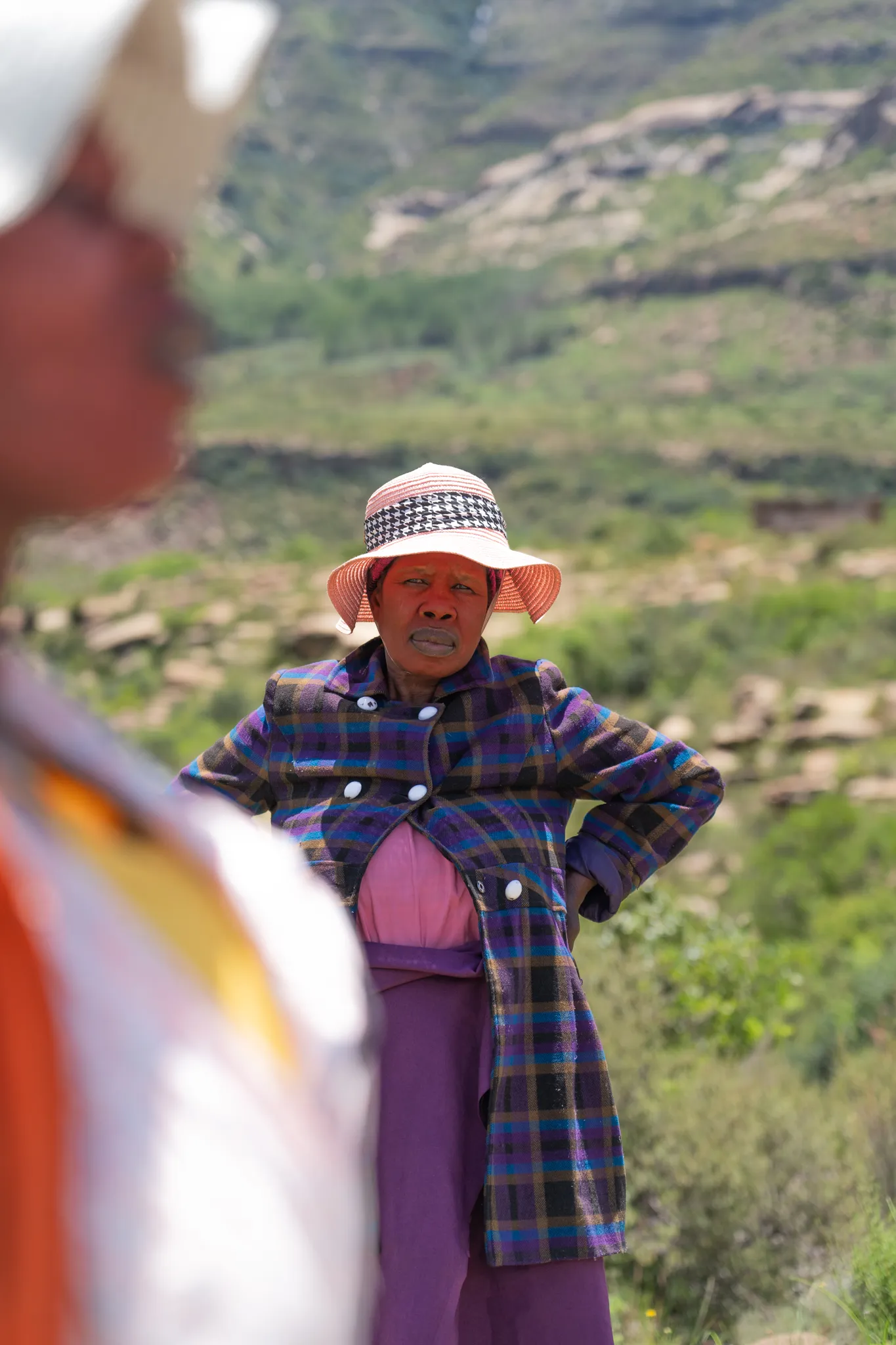 Woman in plaid coat and straw hat, hands on hips