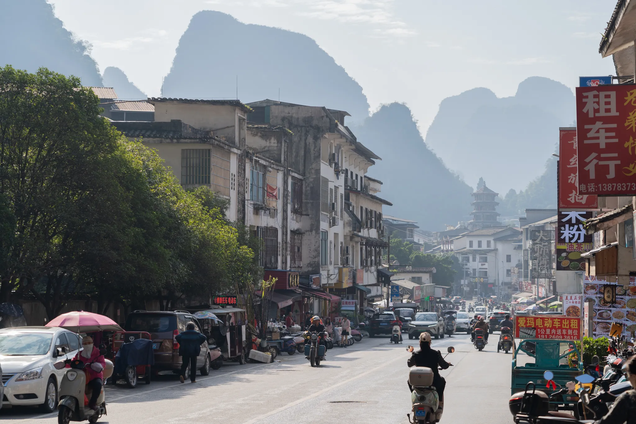 Street traffic beneath limestone peaks and a pagoda